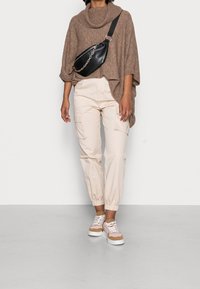 Pull tricoté surdimensionné marron clair avec un col haut, pantalon cargo crème avec poignets élastiques, et baskets multicolores avec une semelle blanche épaisse.