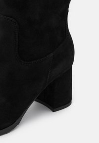 Bottine en daim noir avec bout carré, talon épais, surpiqûres contrastantes et ajustement confortable autour de la cheville.