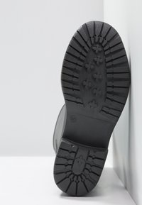 Suela de bota de goma negra con un patrón de relieve texturizado que presenta ranuras alargadas y en forma de cruz para mayor tracción. Tamaño 37 indicado.