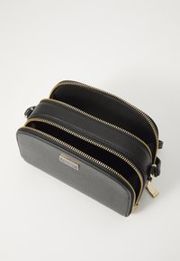 Borsa nera strutturata con doppi scomparti, zip dorate e una finitura testurizzata. Presenta una discreta piastra del marchio sul davanti.