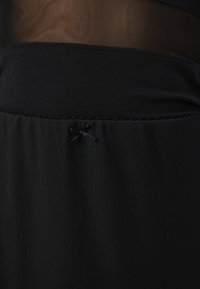 Juoda sluoksniuota apranga, turinti permatomą viršutinę dalį ir tvirtą apatinį audinį. Ant juosmens yra siuvinėtas mažas lankelis.