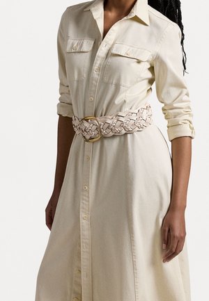 Jasnobeżowa sukienka koszulowa z guzikami z przodu, długimi rękawami i dwoma kieszeniami. Uzupełniona białym plecionym paskiem z złotą okrągłą klamrą.