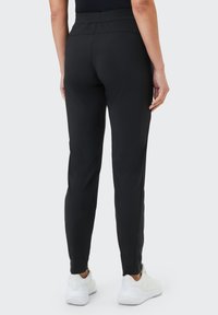 Schwarze, leichte Stretch-Hosen mit schmalem Schnitt, elastischem Bund und knöchellang, kombiniert mit weißen Sportschuhen.