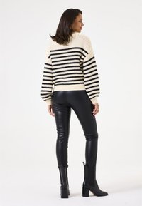 Cream and black striped sweater with a loose fit and ribbed cuffs, paired with black faux leather leggings and heeled black ankle boots.