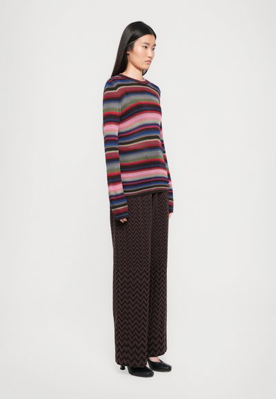 Multifarvet stribet sweater i blød strik, med lange ærmer og rund halsudskæring; parret med mørke zigzag-mønstrede vide bukser.