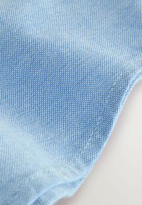 Tela de denim azul claro con un tejido fino, que presenta una textura suave y detalles sutiles de costura a lo largo de los bordes.