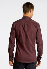 Bordeaux langearmshirt met een subtiele textuurpatroon, voorzien van een button-down kraag en manchetten, een getailleerde pasvorm en een rugplooidetail.
