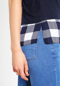 Marinblå t-shirt med rutigt marinblått och vitt fåll, tillverkad av mjukt tyg, kombinerad med ljusblå denimjeans. Synlig sömnad och fickdetaljer.