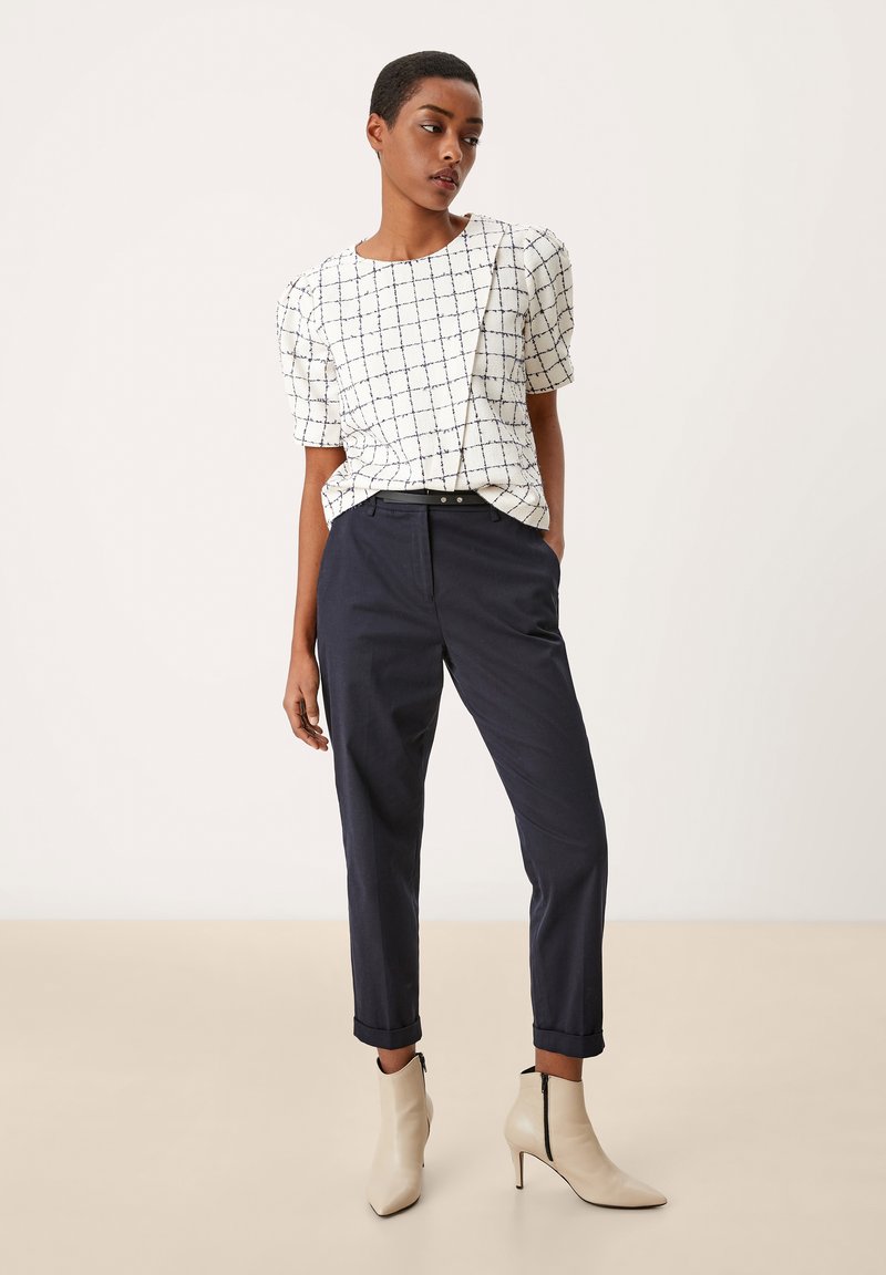 Haut blanc avec motif en grille marine, manches courtes bouffantes ; pantalon bleu foncé tapered ; bottines beiges pointues à détail zip.