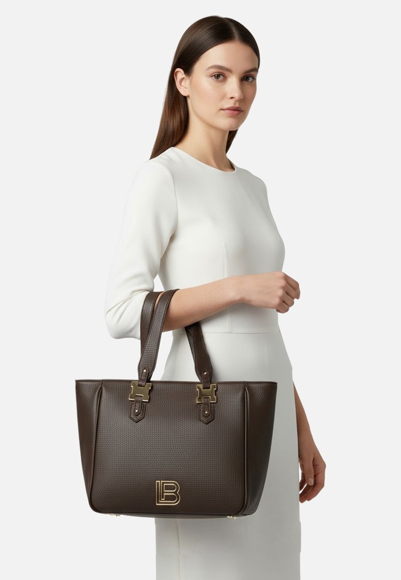 Borsa marrone con trama, dotata di doppio manico, rifinita con dettagli in metallo color oro e logo in rilievo. Fianchi lisci con forma rettangolare.