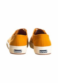 Sneaker gialli in tela con tomaia testurizzata, suole in gomma bianca e un'etichetta con il marchio sul tallone. Vista posteriore con forma arrotondata e profilo basso.
