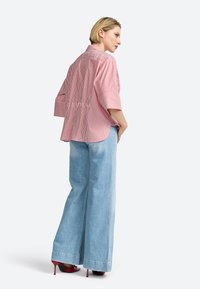 Camicia a righe rosse e bianche con maniche corte, orlo curvo e vestibilità relax, abbinata a jeans a gamba larga blu chiaro e tacchi rossi.