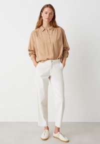 Camicia button-up marrone chiaro con colletto, abbinata a pantaloni bianchi. Tessuto morbido con vestibilità rilassata e maniche arrotolate.