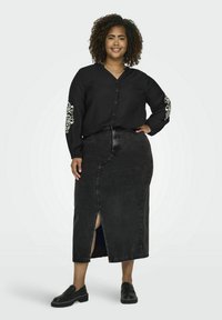 Cămașă neagră cu butoni, decorată cu broderie florală pe mâneci, purtată cu o fustă din denim neagră, cu talie înaltă, care are o fendue frontală și loafers negri.