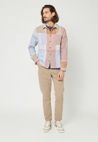 Camicia a quadri leggera con tonalità blu, beige e pesca, con chiusura a bottoni, due tasche sul petto e colletto, abbinata a pantaloni beige e sneakers.