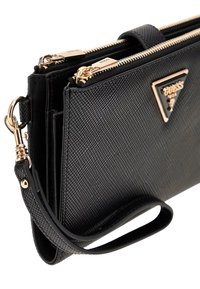 Sort tekstureret syntetisk taske med hardware i guldtoner, dobbelte lynlåse og et logo-plakette. Har en aftagelig håndledsrem til bæring.