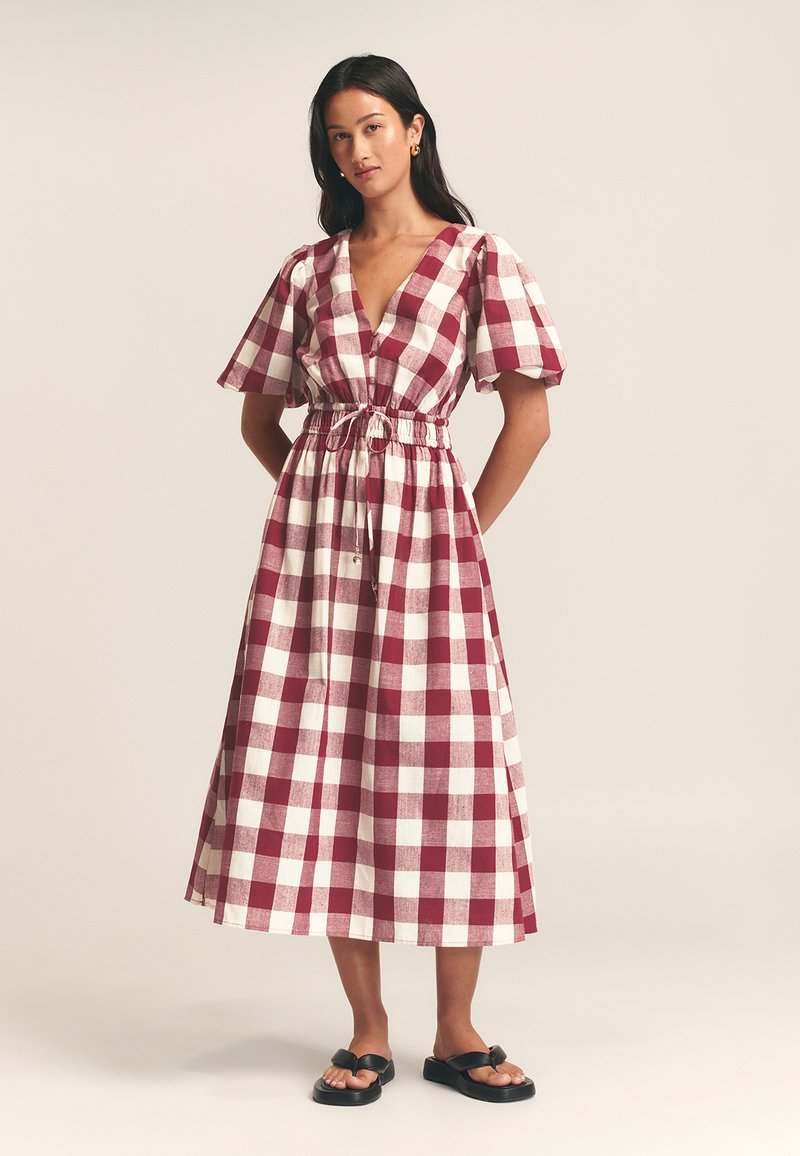 Maxi sukienka w czerwono-białą kratę, z głębokim dekoltem w kształcie litery V, bufiastymi rękawami, zwężoną talią z sznurkiem i długością do kostek.