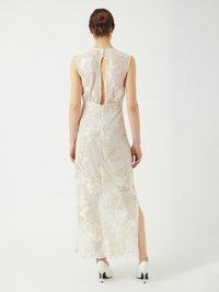 Vue arrière d'une robe sans manches brodée de fleurs en beige clair, avec un détail en trou de serrure et une fente sur le côté, assortie de talons hauts blancs.