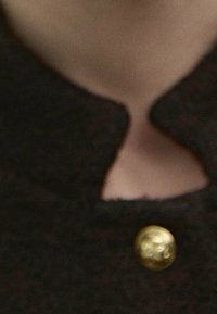 Black wool garment featuring a small keyhole neckline and a gold button accent near the collar. Textured fabric with a sleek design.