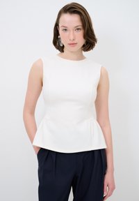 Weißes Peplum-Oberteil mit ärmellosem Design und glatter Textur, kombiniert mit navyblauen Hosen, die durch klare Linien und einen minimalistischen Stil bestechen.