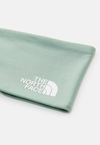 Pehmeä vihreä kangasotsapanta, jossa on uurrettu pintakuvio ja valkoinen logo, jossa lukee "The North Face" ja puoliympyräkuvio toisella puolella.