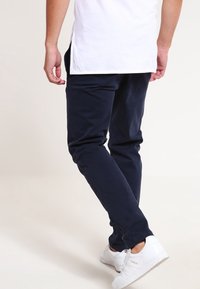 Marina blå byxor i slim fit med en slät yta och sidofickor, bar tillsammans med vita sneakers och en enfärgad vit T-shirt.