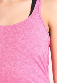 Rosa atletisk linne i mjukt, strukturerat tyg, med en rundad halsringning och tunna axelband lager på lager över ett svart plagg.