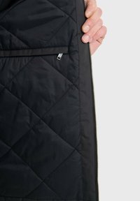Schwarze gesteppte Jackeninnenseite mit sichtbarem Reißverschlussfach, glatter Textur und kontrastierender heller Fütterung entlang des Reißverschlusses.