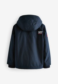 Giacca a vento impermeabile blu navy con cappuccio, dotata di polsini a coste, patch con logo sulla parte superiore della schiena e una texture liscia.