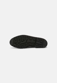 Suela de zapato de goma negra con un patrón texturizado de agarre, que presenta ranuras profundas y un borde frontal redondeado para una mayor tracción.