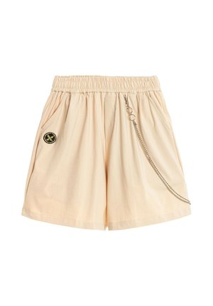 Pantalones cortos beige con cintura elástica, bolsillos laterales, un parche circular negro y amarillo en el lado izquierdo, y una cadena plateada colgando en el lado derecho.