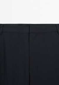 Pantaloni neri con una texture di tessuto liscia, taglio dritto e dettagli di cucitura minimi in vita e sulle cuciture.