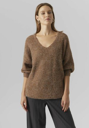 Maglione lavorato a maglia marrone, con scollo a V e maniche ampie, abbinato a pantaloni a righe. Aspetto morbido e vestibilità rilassata.