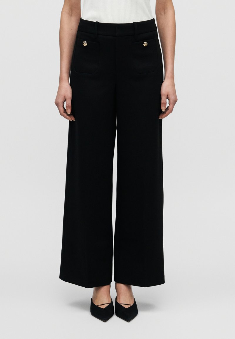 Pantaloni neri a gamba larga con una texture liscia, caratterizzati da due tasche frontali e dettagli con bottoni dorati. Vita sagomata per una vestibilità perfetta.