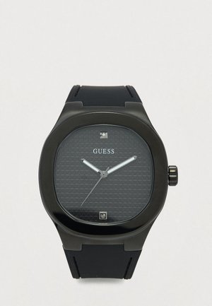 Black Guess wristwatch with textured dial, silver hands, black strap, and two small square markers at 12 and 6 o'clock positions.