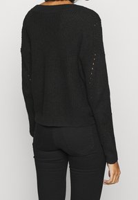 Czarny sweter dziany o luźnym kroju, opuszczonych ramionach i otwartych oczkach na rękawach. Teksturowana tkanina z krótkim ściągaczem.