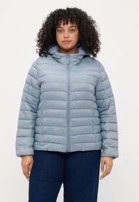 Gaiši zila pūkainā jaka ar pievilkšanai paredzētu rāvējslēdzēju priekšā, kapuci un ribotām piedurknēm. Iespējošs kvadrātveida tekstūra un gluda auduma izolācijai.