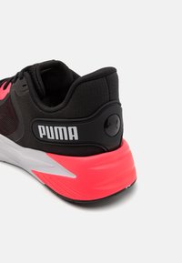 Černá a růžová sportovní obuv Puma s bílou podrážkou, polstrovaným límcem, síťovanými bočními panely a logem Puma na patě a pásku na patě.