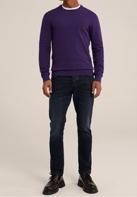 Lila rundhalsad tröja gjord av stickad tyg, parat med mörkblå slim-fit jeans och svarta snörskor med en robust sula.