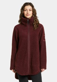 Burgundy fleecetröja med hög krage och full dragkedja. Har långa ärmar och rundad nederkant. Mjuk, strukturerad yta. Enkel design.