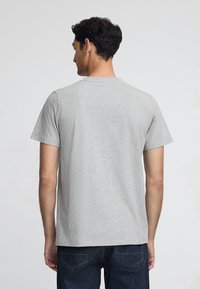 Grijze T-shirt met korte mouwen en ronde hals, met een gladde textuur. Draagt met donkere denim jeans, die een casual pasvorm van de achterkant laten zien.