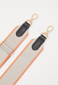 Nastavitelný řemínek ze šedé tkaniny s oranžovými pruhy, zakončený černými koženými konci a zlatými kovovými sponami pro upevnění.