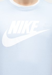 Άνδρας που φοράει ένα ανοιχτό γαλάζιο βαμβακερό T-shirt με μεγάλο λευκό λογότυπο της Nike στο στήθος.