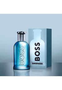 Sininen lasinen BOSS-hajuvesipullo hopeakorkilla, vieressään vastaava laatikko, jossa lukee "BOSS Bottled Tonic Eau de Toilette."