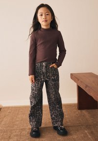 Top marrón de manga larga con textura acanalada, combinado con jeans de talle alto con estampado de leopardo en gris. Zapatos negros gruesos completan el conjunto.