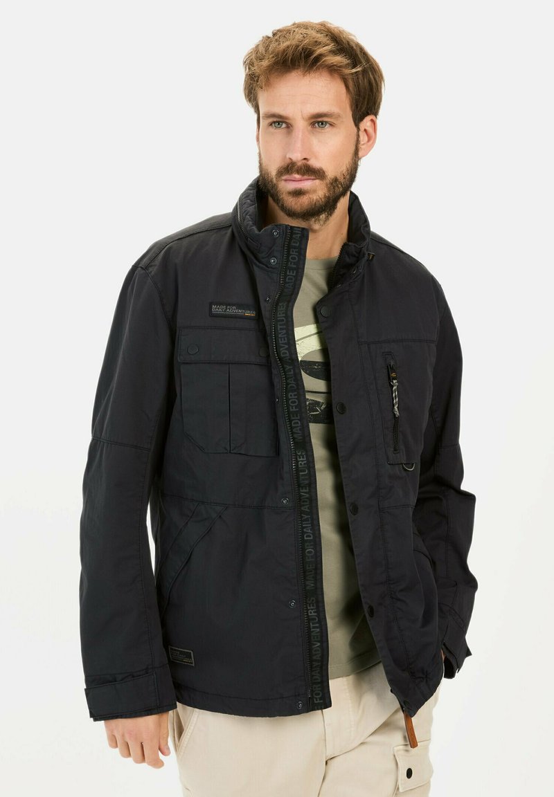 Schwarze, gepolsterte Jacke mit hohem Kragen, mehreren Taschen und Reißverschluss. Strukturierter Stoff und dezentes Branding-Detail auf der Vorderseite.