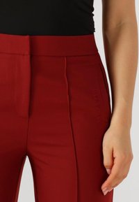 Rode op maat gemaakte broek met een gladde textuur, voorzien van een hoge taille, zijzakken en een reliëflogo aan de voorkant.