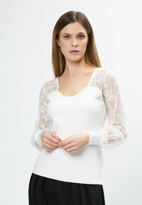 Weißer Pullover mit Spitzen-Puffärmeln, mit U-Boot-Ausschnitt und gerippten Bündchen. Glatte Textur, taillierter Schnitt und kontrastierender schwarzer Rock.