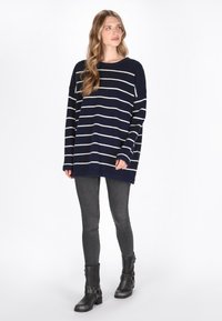 Sweter w granatowe paski z długimi rękawami, luźny kroj, okrągły dekolt, w połączeniu z szarymi slim fit dżinsami i czarnymi botkami za kostkę.