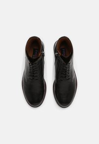 Botas de cuero negro con una textura suave, que presentan un diseño de cordones y un zip lateral, con forro interior marrón y suela marrón en contraste.